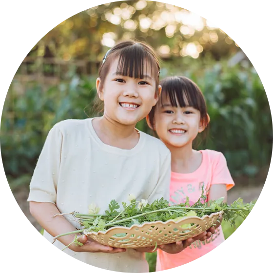 Two young girls holding a basket of vegetables.