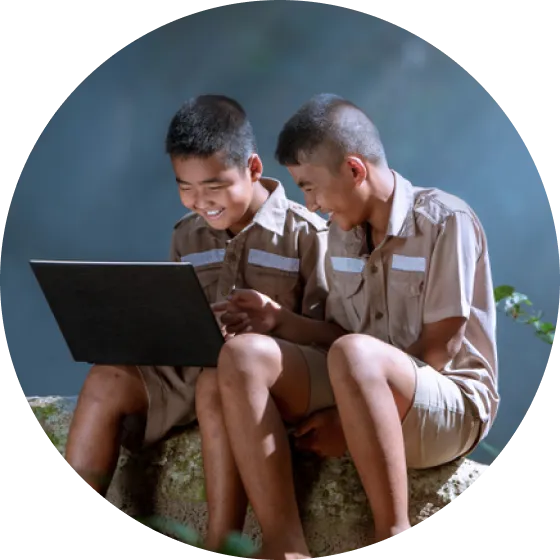 Two men sitting on a rock looking at a laptop.